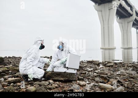 Porträt von zwei Arbeitern in Gefahrgutanzügen, die Probenproben mit Wasser sammeln, Konzept für giftigen Abfall, Kopierraum Stockfoto