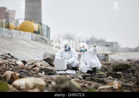Porträt von zwei Arbeitern in Gefahrgutanzügen, die Probenproben im industriellen Bereich sammeln, Konzept für toxische Abfälle Stockfoto