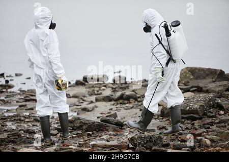 Porträt von zwei Arbeitern in Gefahrgutanzügen, die Probenproben mit Wasser und giftigen Abfällen sammeln Stockfoto