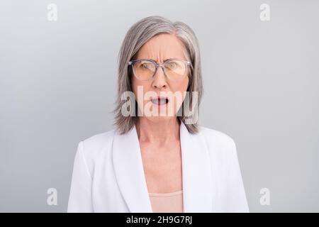 Foto von Angst weiße Frisur gealterte Dame offenen Mund tragen Brillenjacke isoliert auf grauem Hintergrund Stockfoto