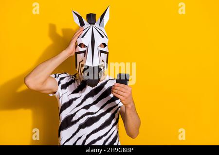 Foto von überrascht Kerl in Zebra Maske lesen Medien News Smartphone berühren Hand Kopf isoliert über hellen gelben Hintergrund Stockfoto