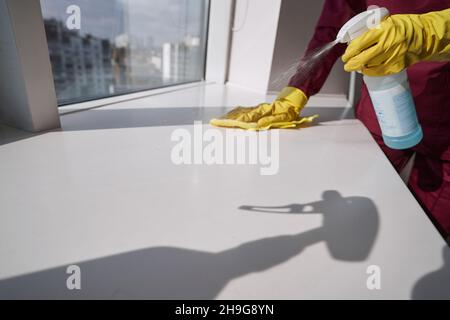 Reinigen Sie die Fensterbank mit einem feuchten Lappen in Gummihandschuhen Stockfoto