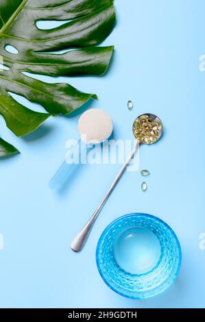 Kollagen-Protein-Pulver im Messlöffel, Vitaminkapseln, Glas reines Wasser auf blauem Hintergrund. Natürliche Schönheit und Gesundheit Ergänzung für Ski Stockfoto