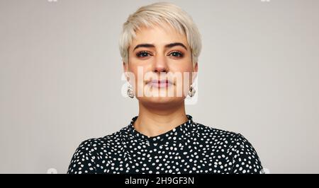 Porträt einer blonden Frau, die allein in einem Studio steht. Nahaufnahme einer modischen Frau mittleren Erwachsenen, die selbstbewusst auf die Kamera schaut, während sie wieder steht Stockfoto