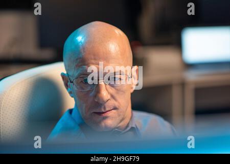 Leiter des reifen kahlen IT-Managers oder Programmierers, der Daten auf dem Computerbildschirm betrachtet, während er im Büro arbeitet Stockfoto