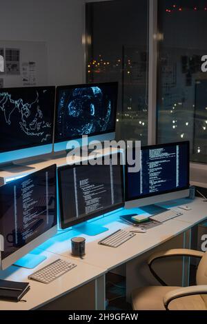 Gruppe von Computermonitoren mit codierten Daten, die nachts auf Schreibtischen im leeren Büro des Programmierunternehmens stehen Stockfoto