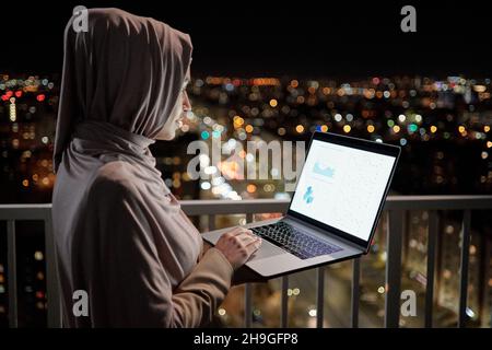 Junge Wirtschaftswissenschaftlerin analysiert das Finanzdiagramm auf dem Laptop-Bildschirm, während sie spät in der Nacht arbeitet Stockfoto