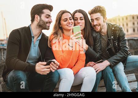 Junge Leute, Freunde, die sich sorglos Social-Media-Inhalte auf dem Smartphone-Bildschirm ansehen - Millennials, die Spaß mit Technologien haben, die im Freien sitzen Stockfoto
