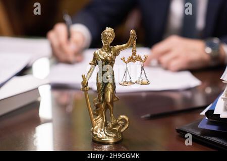 Statue von Lady Justice mit gefesselten Augen, die Waage gegen die Hände eines zeitgenössischen Rechtsanwalts hält, der Papiere unterschreibt Stockfoto