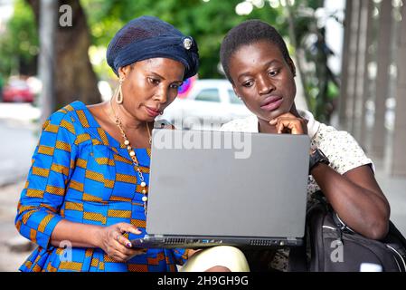 Schöne Geschäftsfrauen, die im Freien sitzen und mit einem Laptop arbeiten. Stockfoto
