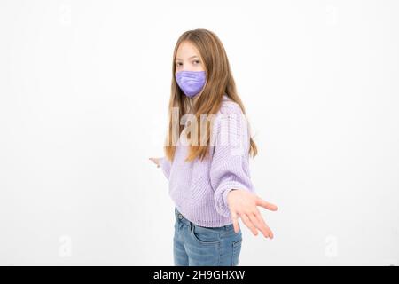 Ziemlich blonde Mädchen in lila Wolle Pullover mit Nase Mund Maske steht vor weißem Hintergrund Stockfoto