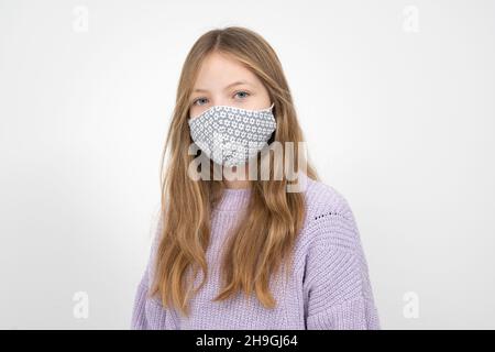 Ziemlich blonde Mädchen in lila Wolle Pullover mit Nase Mund Maske steht vor weißem Hintergrund Stockfoto