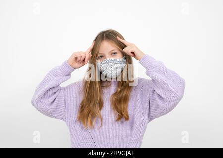 Ziemlich blonde Mädchen in lila Wolle Pullover mit Nase Mund Maske steht vor weißem Hintergrund Stockfoto