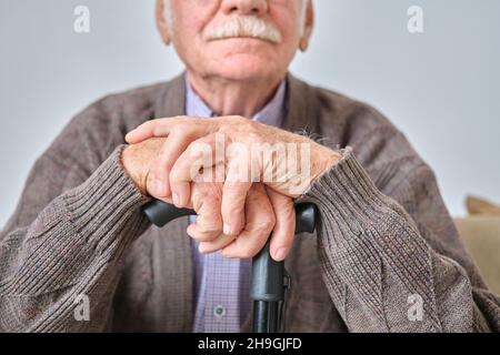 Nahaufnahme eines älteren Mannes mit weißem Schnurrbart, der auf seiner Krücke sitzt Stockfoto