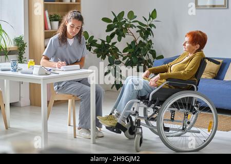 Ärztin, die die Behandlung für ältere Frauen verschreibt, die im Rollstuhl sitzen und einen Arzt im Krankenhaus besuchen Stockfoto