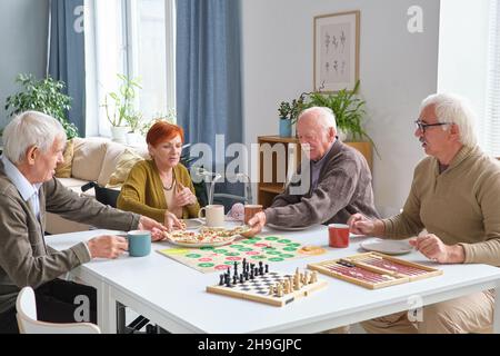 Eine Gruppe älterer Freunde, die nach einem Brettspiel im Wohnzimmer Pizza am Tisch essen Stockfoto