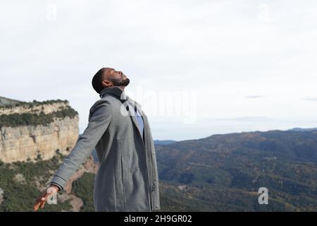 Entspannter Mann mit schwarzer Haut, der im Winter in der Natur frische Luft atmet und eine Jacke trägt Stockfoto