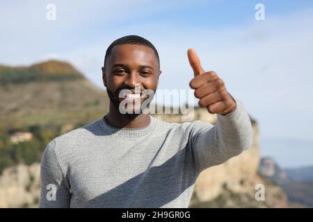 Glücklicher Mann mit schwarzer Haut, der den Daumen in den Berg hochsticht Stockfoto