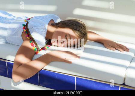 Ein kaukasisches Mädchen im Alter von 11-12 Jahren las ein Buch und schlief ein. Der Teenager ist müde und liegt mit seinem Kopf auf einem offenen Buch auf der Couch. Stockfoto