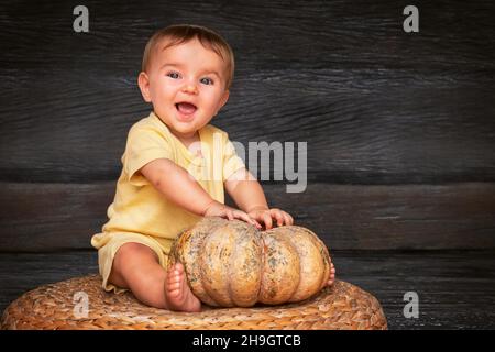 Niedliches Baby mit dem Kürbis lächelnd auf dem Strohtisch auf dem Holzhintergrund Stockfoto