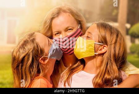 Glückliche Familie trägt die Gesichtsmasken. Maskierte Mädchen küssen glücklich Mutter. Stockfoto