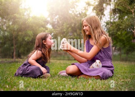 Zwei Mädchen im Park spielen mit Kaninchen. Kinder auf dem Gras Stockfoto