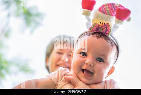 Großmutter hält Enkelin. Frau spielt mit Baby. Kind trägt weihnachtshut lächelnd Stockfoto