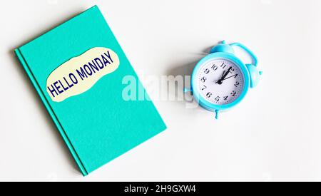 Hallo montag Grünes Tagebuch mit den Worten Hallo montag auf einem Tisch mit Wecker und weißem Hintergrund. Stockfoto