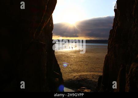 Silhouetten am Ufer oder an der Küste, die bei Sonnenuntergang durch verdunkelte Klippen gesehen werden (Marazion, Cornwall, England) Stockfoto