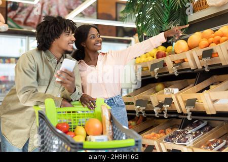 Fröhlicher Afrikanischer Ehemann Und Ehefrau, Die Sich Für Bio-Früchte Im Supermarkt Entscheiden Stockfoto