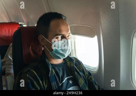 Passagiere mit Masken auf einem Flug der Fluggesellschaft. Während des Ausbruchs des Corona-Virus reisen Menschen weniger und setzen immer chirurgische Masken an. Mann mit Klemme ma Stockfoto