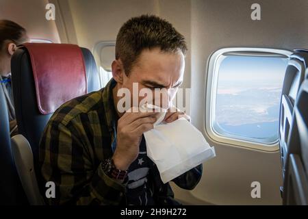 Nervöser junger Mann mit Aviophobie, der im Flugzeug in den Papierbeutel atmet. Übelkeit während des Fluges. Ein junger Mann wird beim Transport carsick. Stockfoto