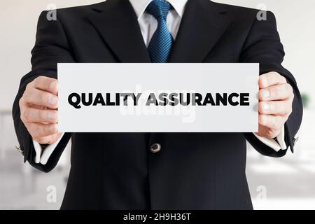 Geschäftsmann zeigt ein Banner mit der Botschaft Qualitätssicherung. Konzept der Qualitätsgarantie für Business-Produkte oder -Dienstleistungen. Stockfoto