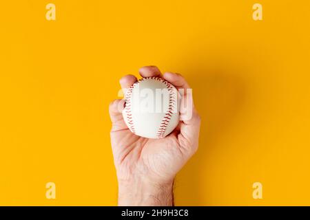 Die männliche Hand hält einen Baseballball auf gelbem Hintergrund. Draufsicht. Stockfoto