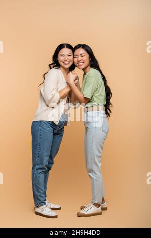 In voller Länge glücklich asiatische Mutter und Tochter hält die Hände auf beige Stockfoto