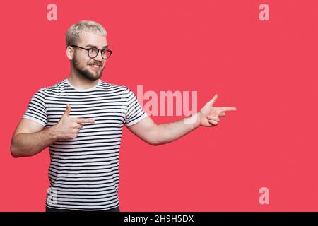 Porträt eines bärtigen Mannes, der auf einen über rosa Hintergrund isolierten Kopierbereich zeigt. Lächelndes Gesicht. Stockfoto
