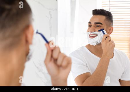 Porträt Eines Hübschen Jungen Arabischen Mannes, Der In Der Nähe Eines Spiegels Im Badezimmer Rasier Stockfoto
