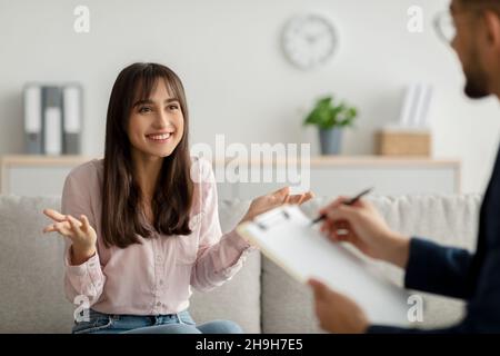 Effektive Psychotherapie. Glückliche arabische Frau, die mit ihrem Psychologen spricht und professionelle Hilfe in der Klinik erhält Stockfoto
