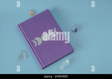 Lilafarbenes Mondphasen-Tagebuch, Chakra-Steine zur Kristallheilung auf blauem Hintergrund. Konzept: Selbstversorgung für die Seele Stockfoto