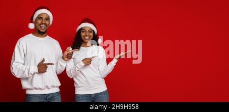 Glückliches afroamerikanisches Paar in Weihnachtsmützen, das Platz für Kopien zeigt Stockfoto