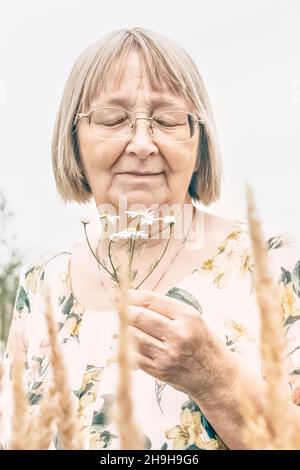Porträt einer älteren Frau mit einem Blumenstrauß, der nach Gänseblümchen riecht. Herbst. Stockfoto