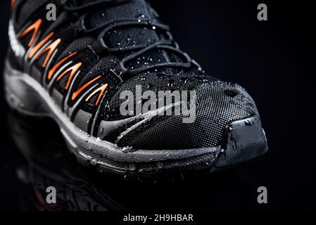 Schwarze Männerstiefel zum Wandern auf dunklem Hintergrund. Wasserdichte Schuhe mit Wassertropfen, Nahaufnahme Stockfoto