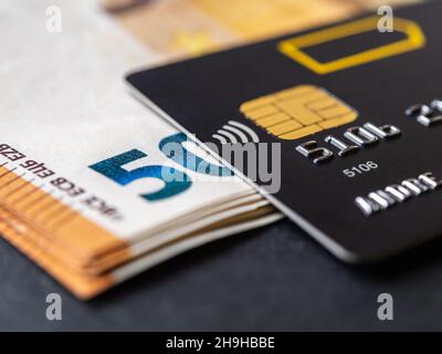 Kreditkarte auf fünfzig Euro-Banknoten Makro. Schwarze Debitkarten für Barabhebungen und Zahlungen für Waren und Dienstleistungen. Bankkarte und Geld. Stockfoto