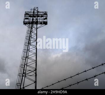 Flutlichter im Sportstadion und Stacheldraht vor stürmischem Himmel. Stockfoto