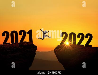 Mann, der bei herrlichem Sonnenuntergang auf der Klippe 2022 über den Abgrund springt. Neujahrskonzept. Symbol für Start und Begrüßung glückliches neues Jahr 2022. Menschen kommen herein Stockfoto