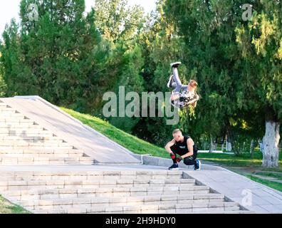 Junger Mann, der gefährliche Sprünge macht, überspringt salto einen anderen Mann, der auf den Stufen des Parks hockte. Stockfoto