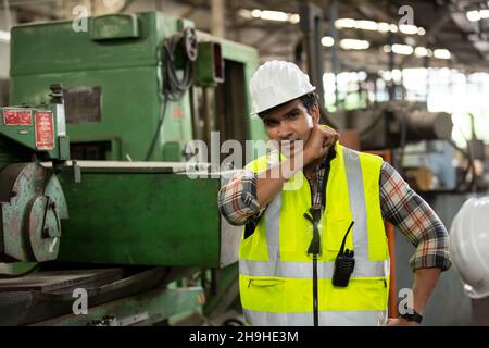 Profilansicht des jungen Technikers im karierten Hemd, das industrielle Maschine inspiziert Stockfoto