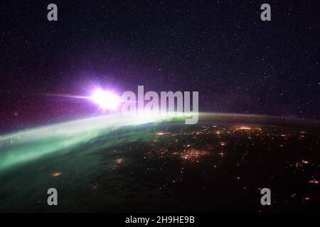 Nachtplanet Erde mit erstaunlichen grünen Polarlichtern und lila Sternenhimmel mit einem hellen Stern. Helle Stadtlichter von Megacities, Blick aus dem All Stockfoto