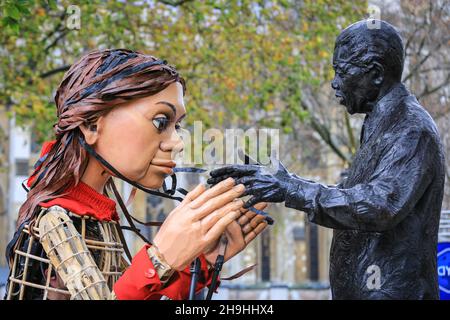 Westminster, London, Großbritannien. 7th Dez 2021. Little Amal mit der Statue von Nelson Mandela auf dem Parliament Square. Die kleine Amal, die riesige Marionette, die ein kleines Flüchtlingsmädchen darstellt, ist heute wieder im Zentrum von London und außerhalb des Parlaments, um einen Protest gegen das Gesetz über Nationalität und Grenzen zu unterstützen, das potenziell Flüchtlinge und andere, die im britischen Asylsystem Asyl suchen, behindern könnte. Die Marionette war in diesem Sommer und Herbst auf einer langen Reise von Syrien nach Großbritannien mit vielen Auftritten unterwegs gewesen. Kredit: Imageplotter/Alamy Live Nachrichten Stockfoto