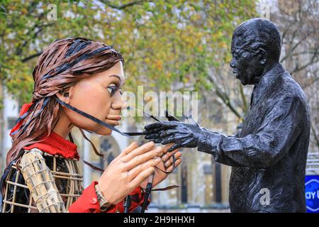 Westminster, London, Großbritannien. 7th Dez 2021. Little Amal mit der Statue von Nelson Mandela auf dem Parliament Square. Die kleine Amal, die riesige Marionette, die ein kleines Flüchtlingsmädchen darstellt, ist heute wieder im Zentrum von London und außerhalb des Parlaments, um einen Protest gegen das Gesetz über Nationalität und Grenzen zu unterstützen, das potenziell Flüchtlinge und andere, die im britischen Asylsystem Asyl suchen, behindern könnte. Die Marionette war in diesem Sommer und Herbst auf einer langen Reise von Syrien nach Großbritannien mit vielen Auftritten unterwegs gewesen. Kredit: Imageplotter/Alamy Live Nachrichten Stockfoto